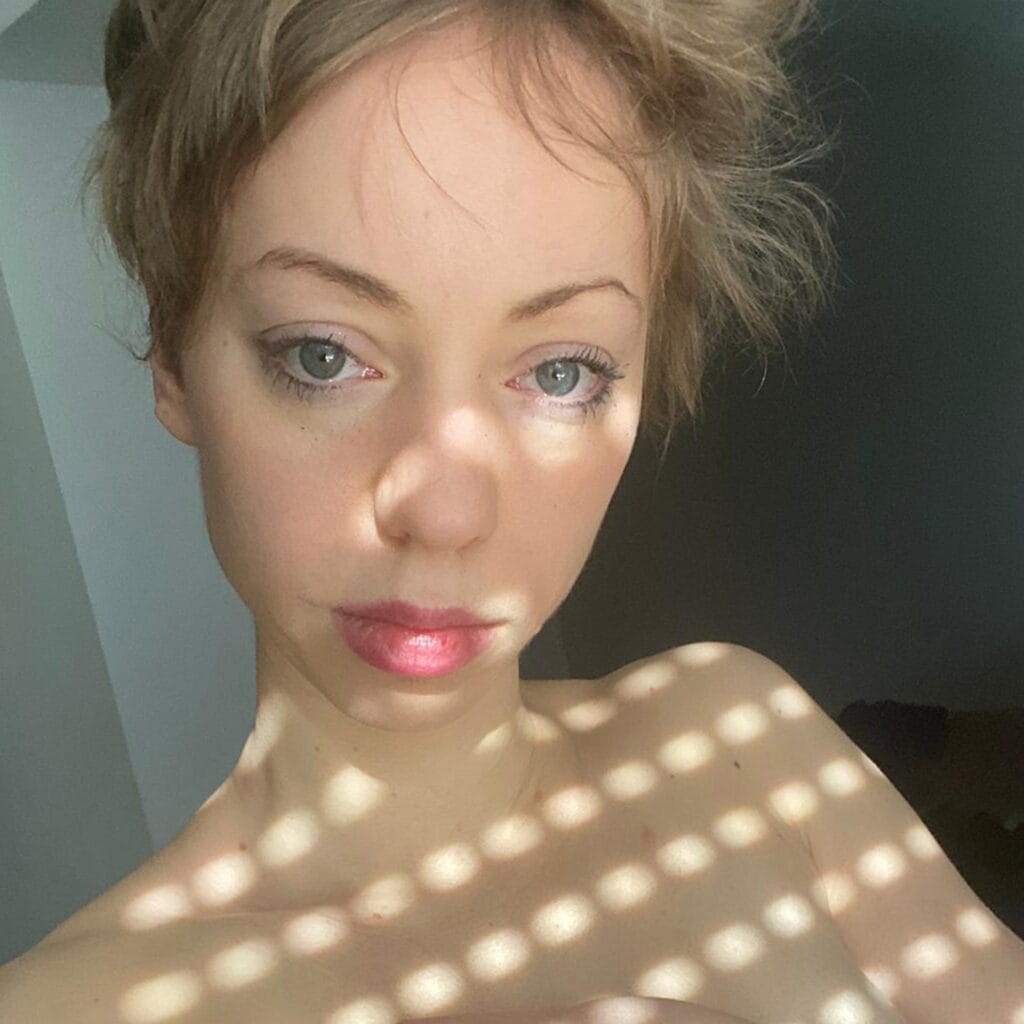 Close-up of a woman's eyes and lips in soft light, with gentle makeup and light dotted shadows across the skin.