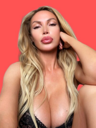 Close-up of a blonde woman resting her head on her hand against a red background, lips glossed.
